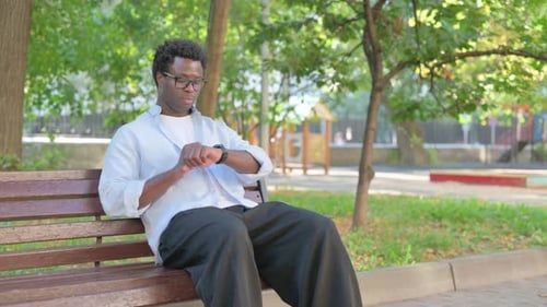 African Man Sitting in the Park and Using Smart Watch