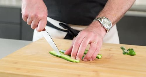 male chef slicing the green cucumber with the tip of the sharp knife
