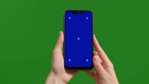 Female holds blue chroma key screen device vertically with fingers on green screen background.