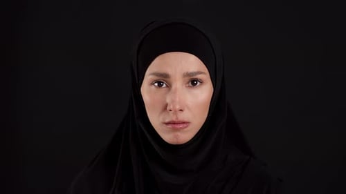 Portrait of Upset Muslim Woman in Traditional Hijab Looking Seriously at Camera Black Studio
