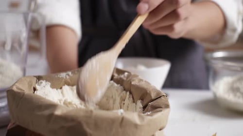 Scooping Flour with Wooden Spoon in Kitchen