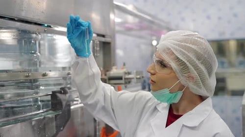 Jeune travailleuse heureuse dans une usine d'embouteillage vérifiant les bouteilles d'eau avant expédition. Qua d'inspection