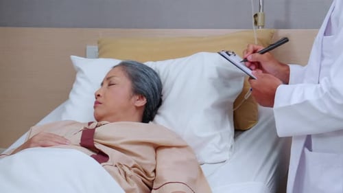 Asian doctor check saline and check patient elderly while asleep on bed at hospital ward.