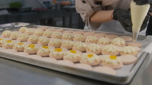 Pastry Chef Piping Cream on Macarons in Kitchen