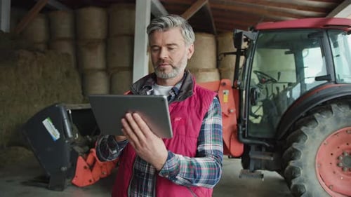 Farmer Using Tablet Inside Barn with Tractor