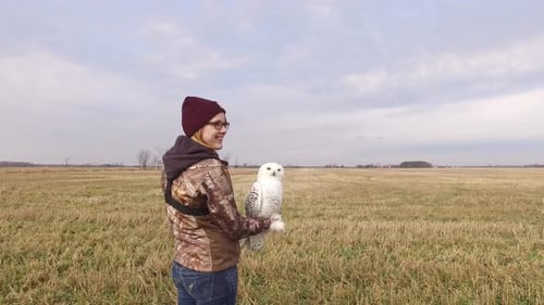 Woman Holds a Snowy Owl in a Field