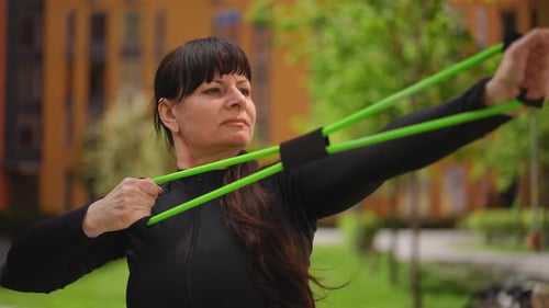 Mulher madura em traje esportivo alonga um expansor flexível enquanto o segura nas mãos que uma mulher está fazendo