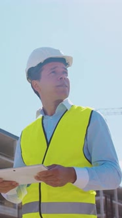 Professioneller Baumeister steht mit Schutzhelm und Weste vor dem Baustellenleiter