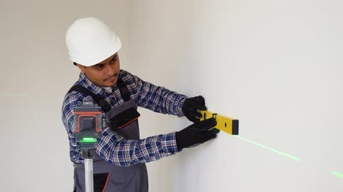 Indian Worker in Measuring Wall with Laser Leveler at Construction Site