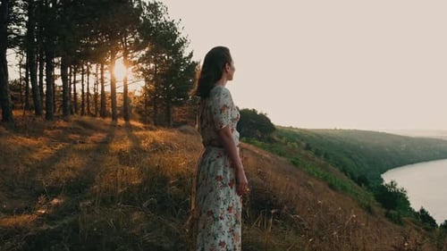 A Woman Dressed in a Beautiful Floral Dress is Gazing at the Stunning Sunset By the River