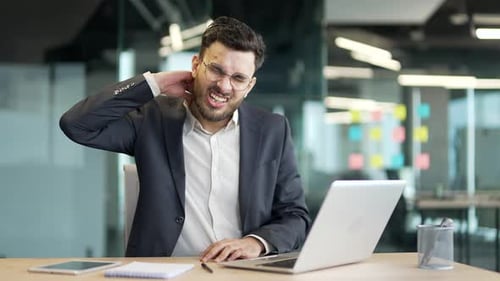 Young Man Massaging Neck Pain at Office Desk