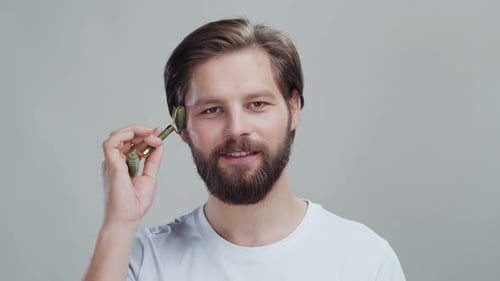 Bearded man using jade facial roller, skincare