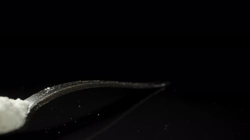 A spoon with a heap of white powder on a black background, illuminated by flickering light, Dolly