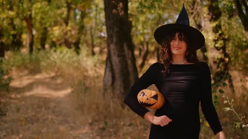 Woman in Witch Costume Waving with Pumpkin