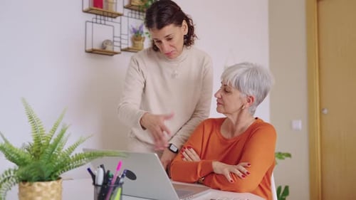 Woman Helping Senior with Laptop at Home Indoors