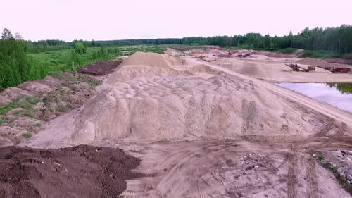 Drone flyover forward over sand quarry and gravel pit with aggregate stockpiles, dirt haul roads