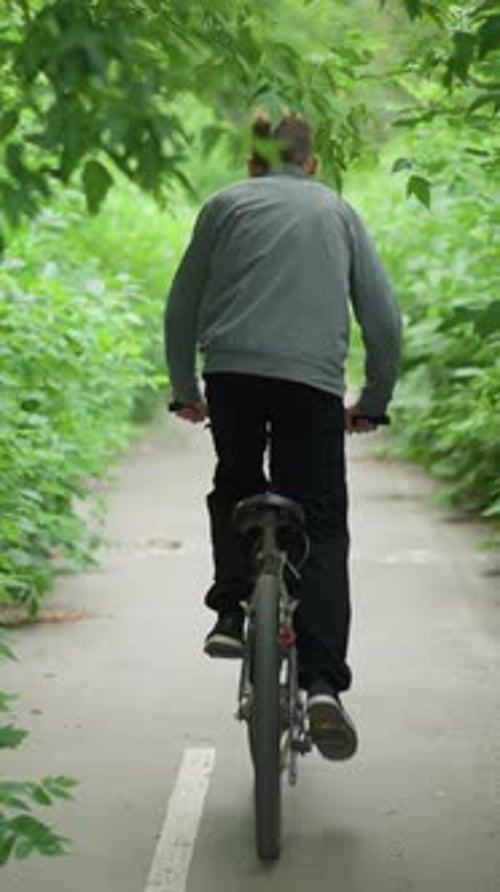 Young Boy Riding Bicycle Through Green Tunnel on Paved Pathway