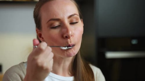 Woman Enjoying a Spoonful of Food in Kitchen