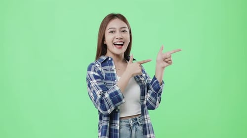 Glückliches schönes asiatisches Mädchen zeigt mit dem Finger und lächelt auf Chroma-Key-Hintergrund.