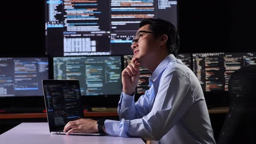 Programmer Thinking About Something While Writing Code By A Laptop Using Multiple Monitors