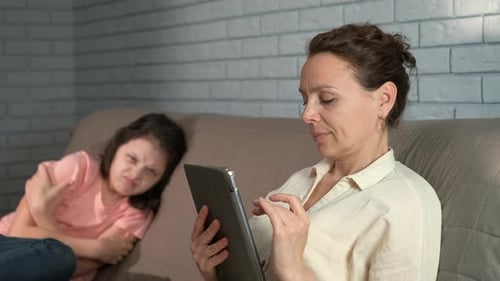 Woman Using Tablet While Girl Frowns in Background