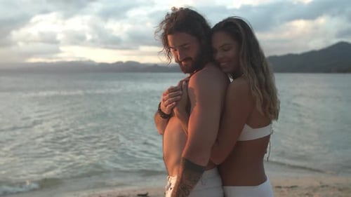 4k video footage of a happy young couple embracing on the beach at sunset