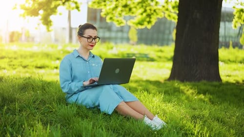 Busy Attractive Woman Working on the Laptop While Sitting on Grass in City Park