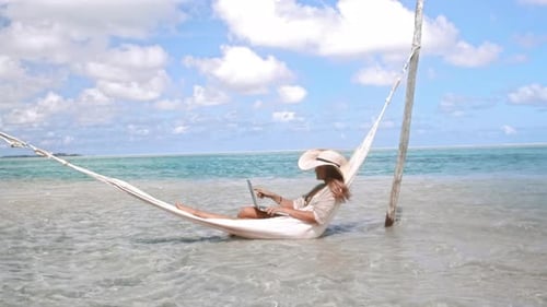 Of Woman Working on Laptop Computer on Hammock in Blue Ocean
