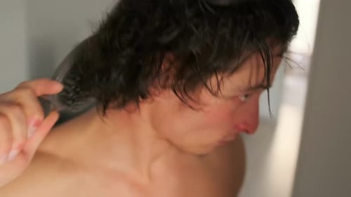 Young Man Brushing Wet Hair in Bathroom Mirror
