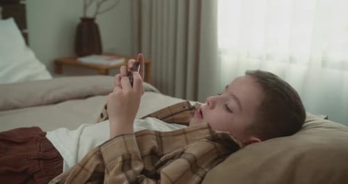 Young Boy Playing on Phone in Bedroom
