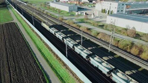 Ein Güterzug, der Kies durch ein Industriegebiet transportiert, wird von einer Drohne verfolgt, die neben dem