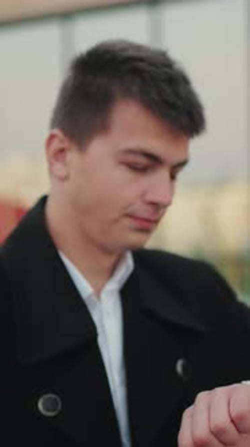Man in Black Coat Checking Time with Confident Look in Front of Glass Building