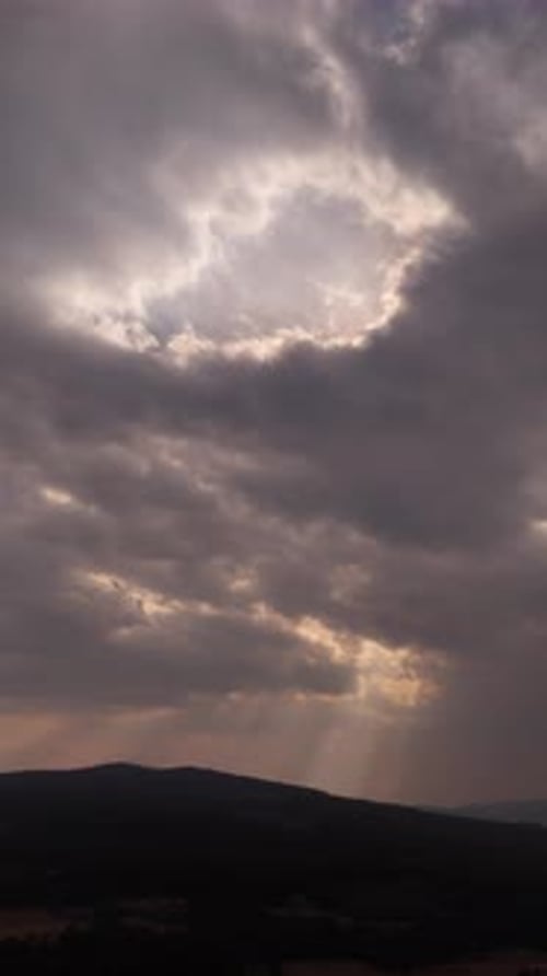 Ciel nuageux à couper le souffle avec des rayons de soleil atteignant les montagnes en dessous - Vertical
