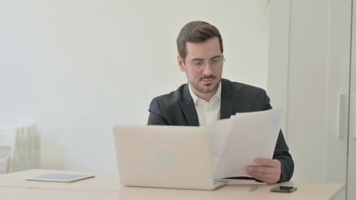 Young Adult Reviews Documents at Desk in Office
