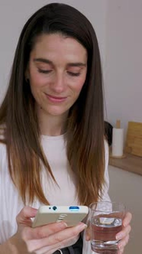Woman Uses Phone While Holding Glass of Water