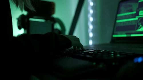 ein kriminelles Hacker-Mädchen mit schwarzer Kapuze, das Laptop und große Computer benutzt, um ihr Netzwerksystem zu hacken
