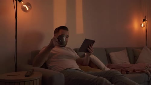 Man Relaxes on Couch Using Tablet at Night