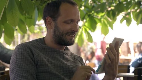 Young Man Using Tablet Computer While Sitting in Cafe 30s