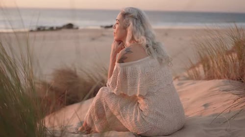 Serene Woman With Gray Hair Sits on Beach at Sunset Contemplating Life