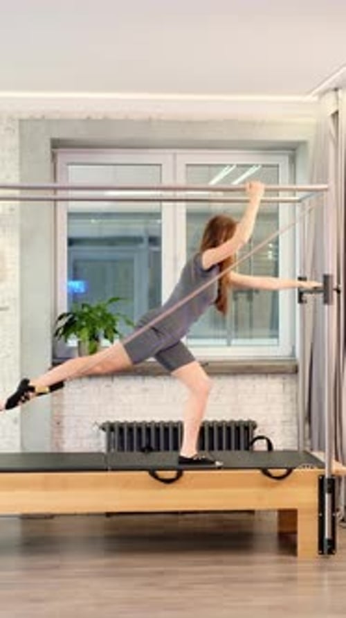 A Woman Performs a Pilates Standing Exercise on a Reformer Tower Maintaining Body Tension and