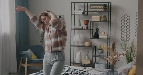 Slow Motion of Carefree Young Woman Listening to Music with Headphones and Dancing Moving in Bedroom