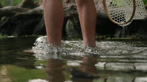 Flyfisherman wading into beautiful green swimming hole splashing in river walking in water to go fis
