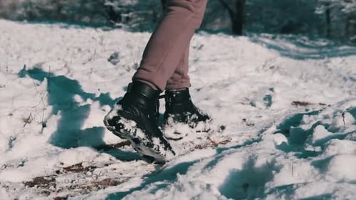 Female Legs with Winter Boots Walking By a Snow Covered Walkway in Winter Forest