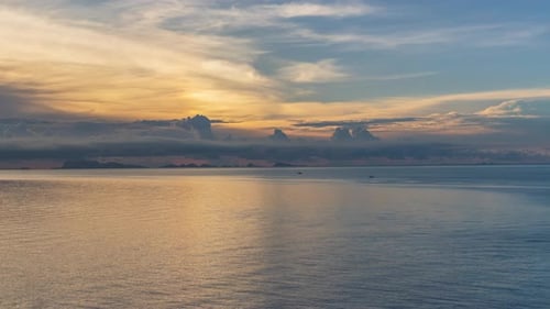 Calm Sea with Soft Sunset Light and Distant Islands Beneath Layered Clouds Creating Warm Golden