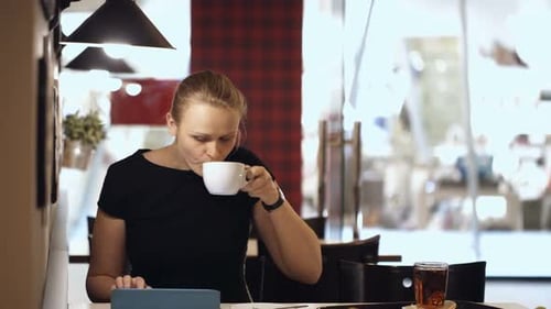 Young woman sitting in cafe with pad and drinking coffee
