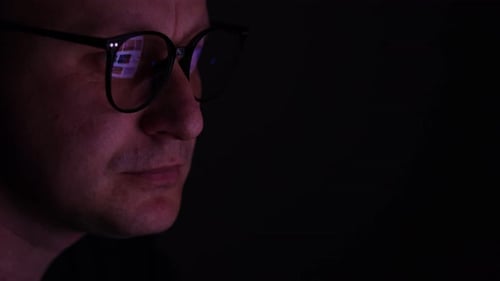 male working online late. Close up side view of focused man wears computer glasses for reducing