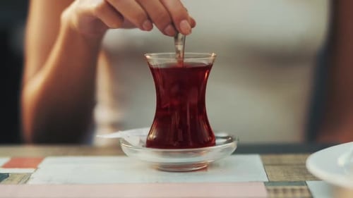 Femme mélangeant du thé noir dans un verre à thé turc traditionnel.