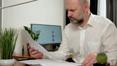 Man Reviews Documents at Desk in Bright Home Office