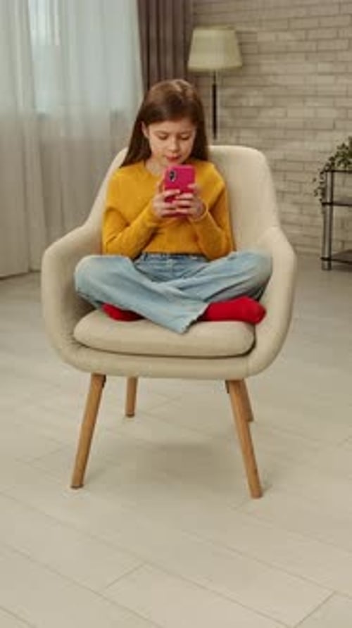 Young Girl Sitting in Chair Using Smartphone Indoors
