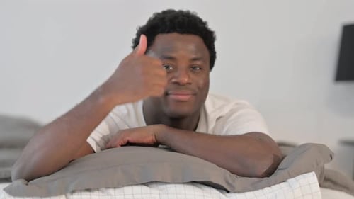 Pouce levé par un homme africain allongé sur le ventre dans son lit